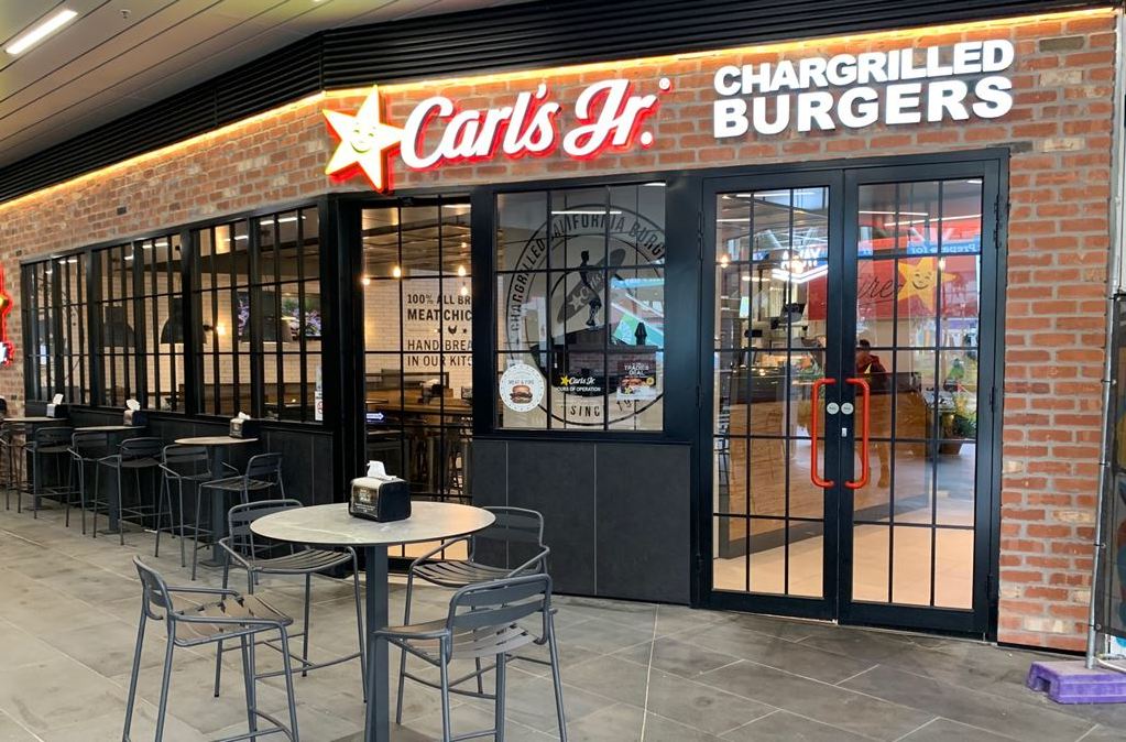A Carl’s Jr. restaurant storefront with brick walls, black-framed windows, and outdoor patio seating.