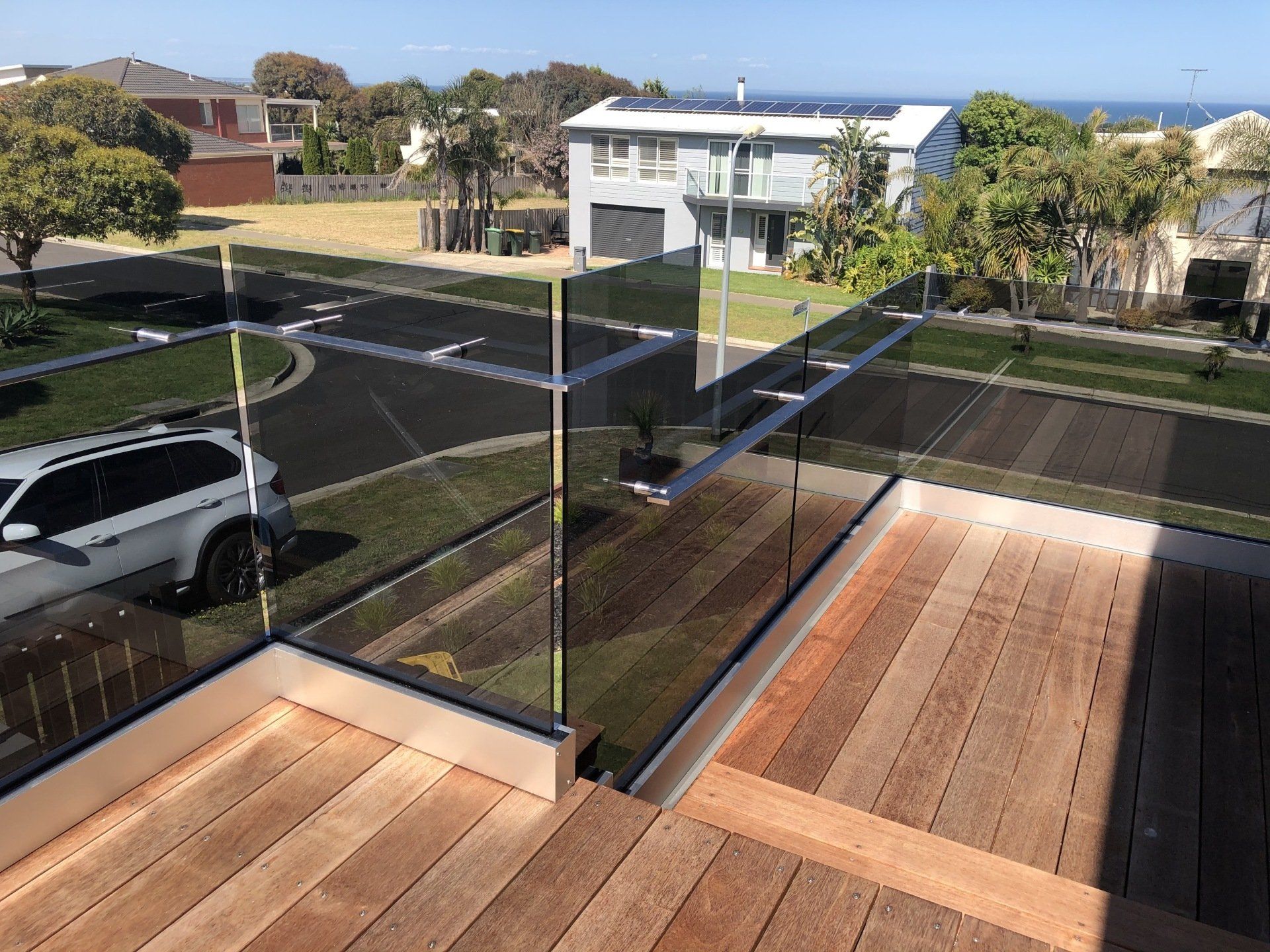 A high-angle view of a wooden deck featuring a glass railing with metal accents, overlooking a street and houses.