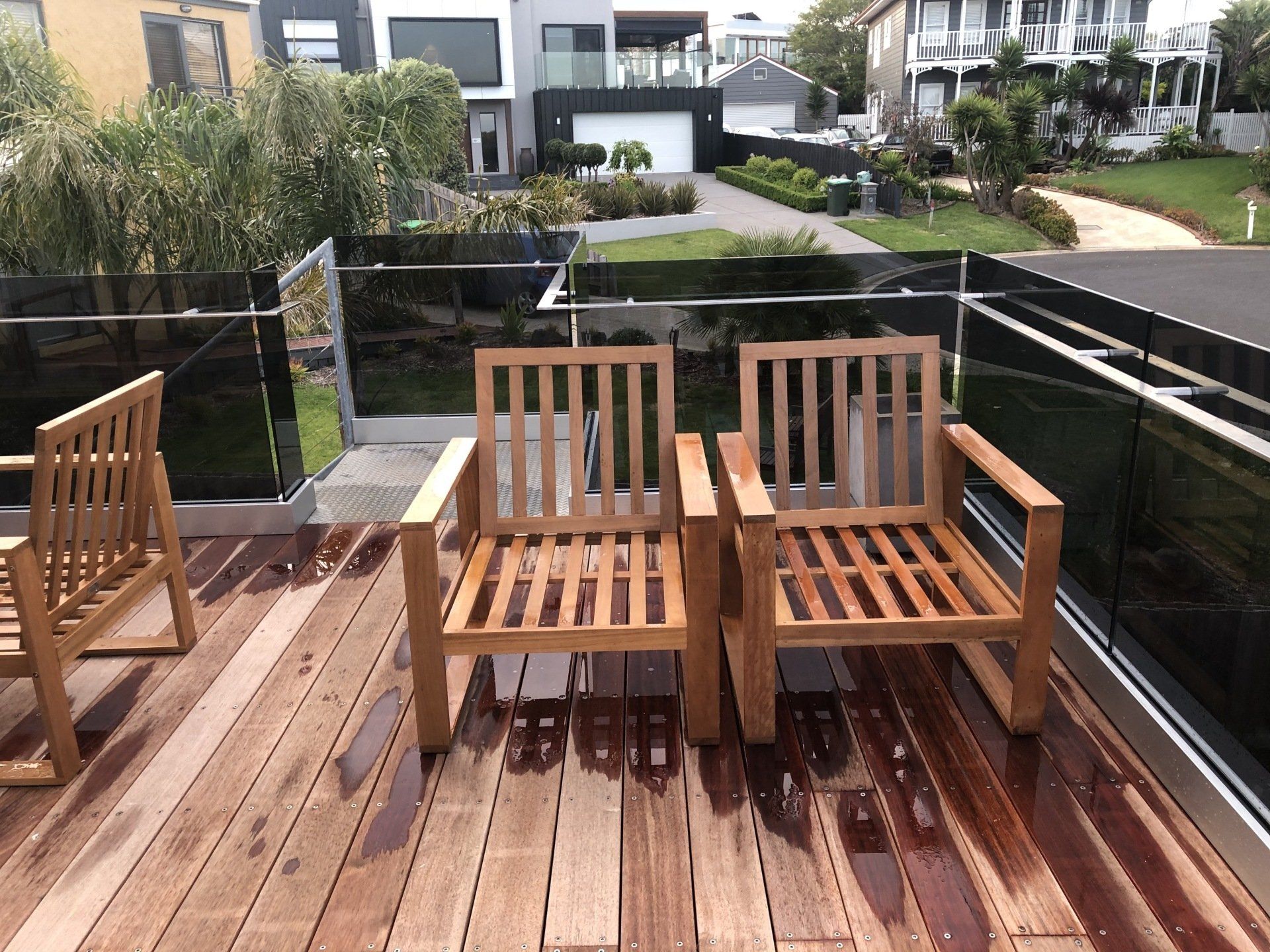 Three wooden chairs arranged on a rain-slicked wooden deck overlooking a suburban neighborhood.
