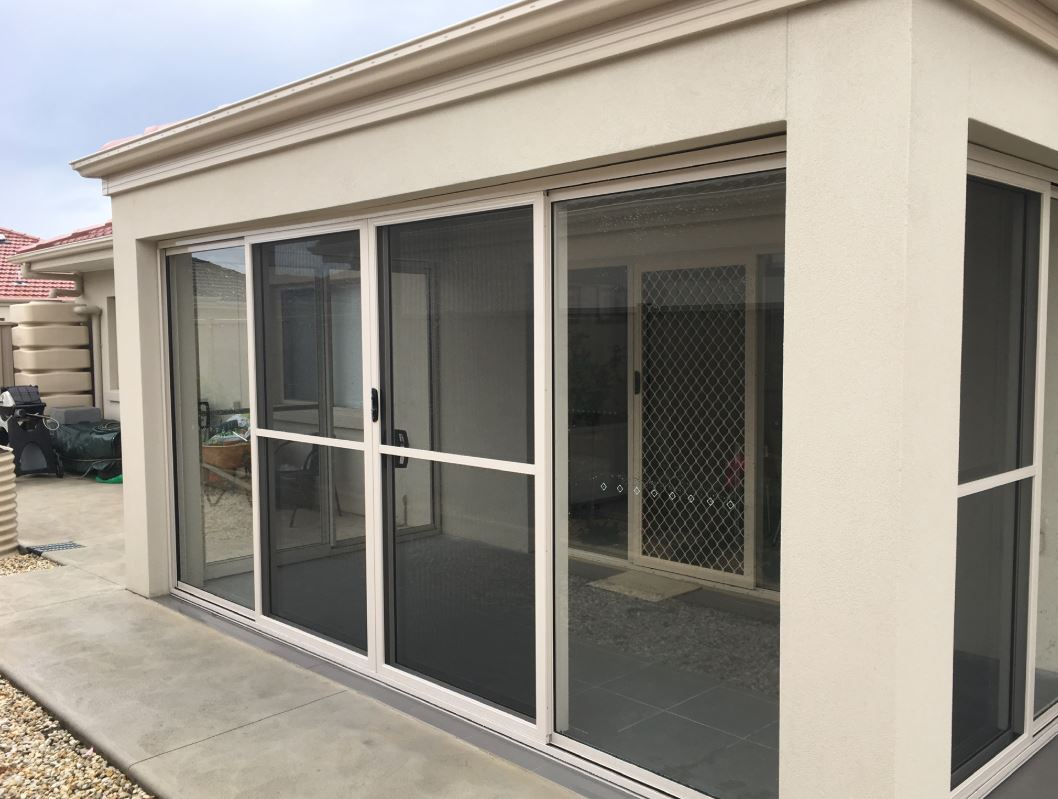 A beige sunroom with sliding screen doors and security screens on an outdoor patio.