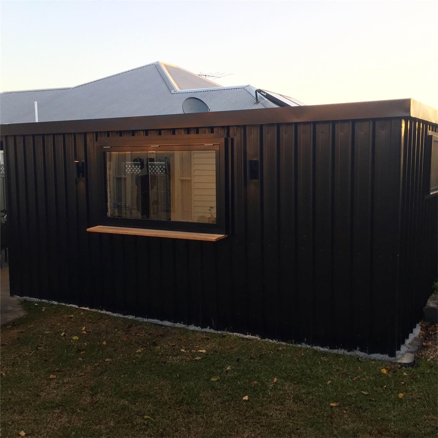 A black, metal-sided rectangular garden shed with a horizontal window and a small wooden exterior ledge.