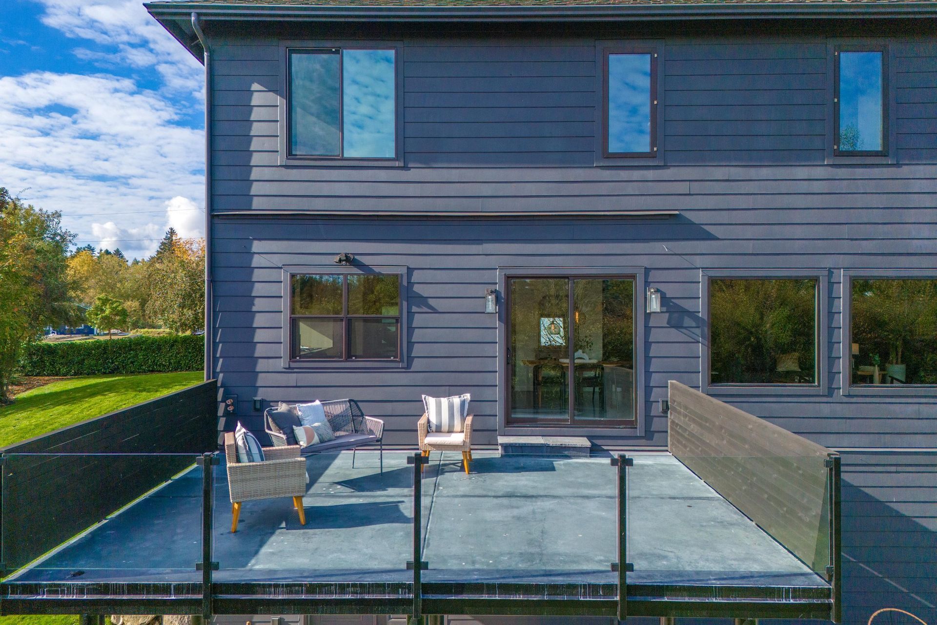 Modern townhouse patio with outdoor seating, glass railing, and sliding doors on a sunny day