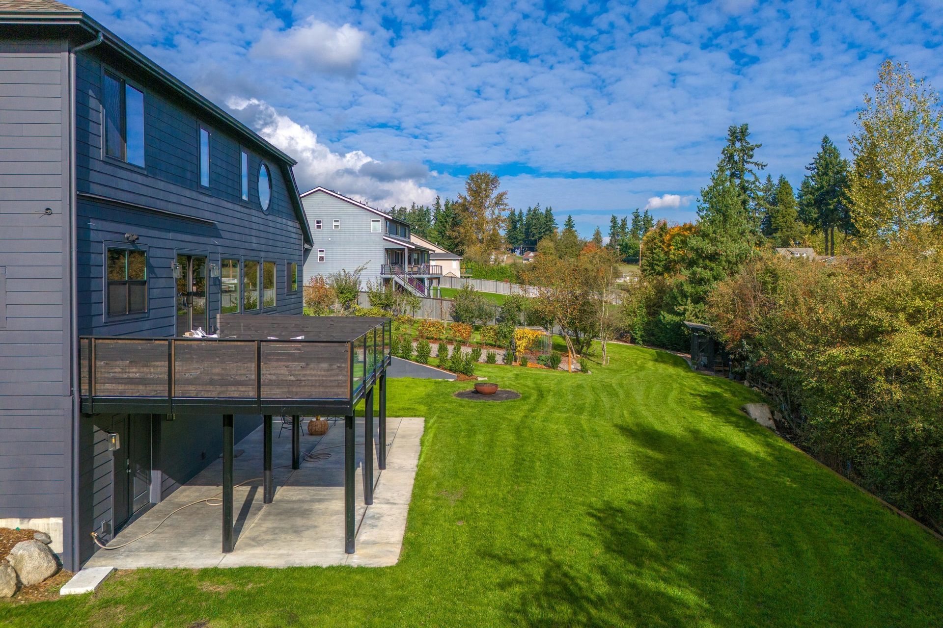 Modern house with wooden deck overlooking a lush green backyard under a blue sky