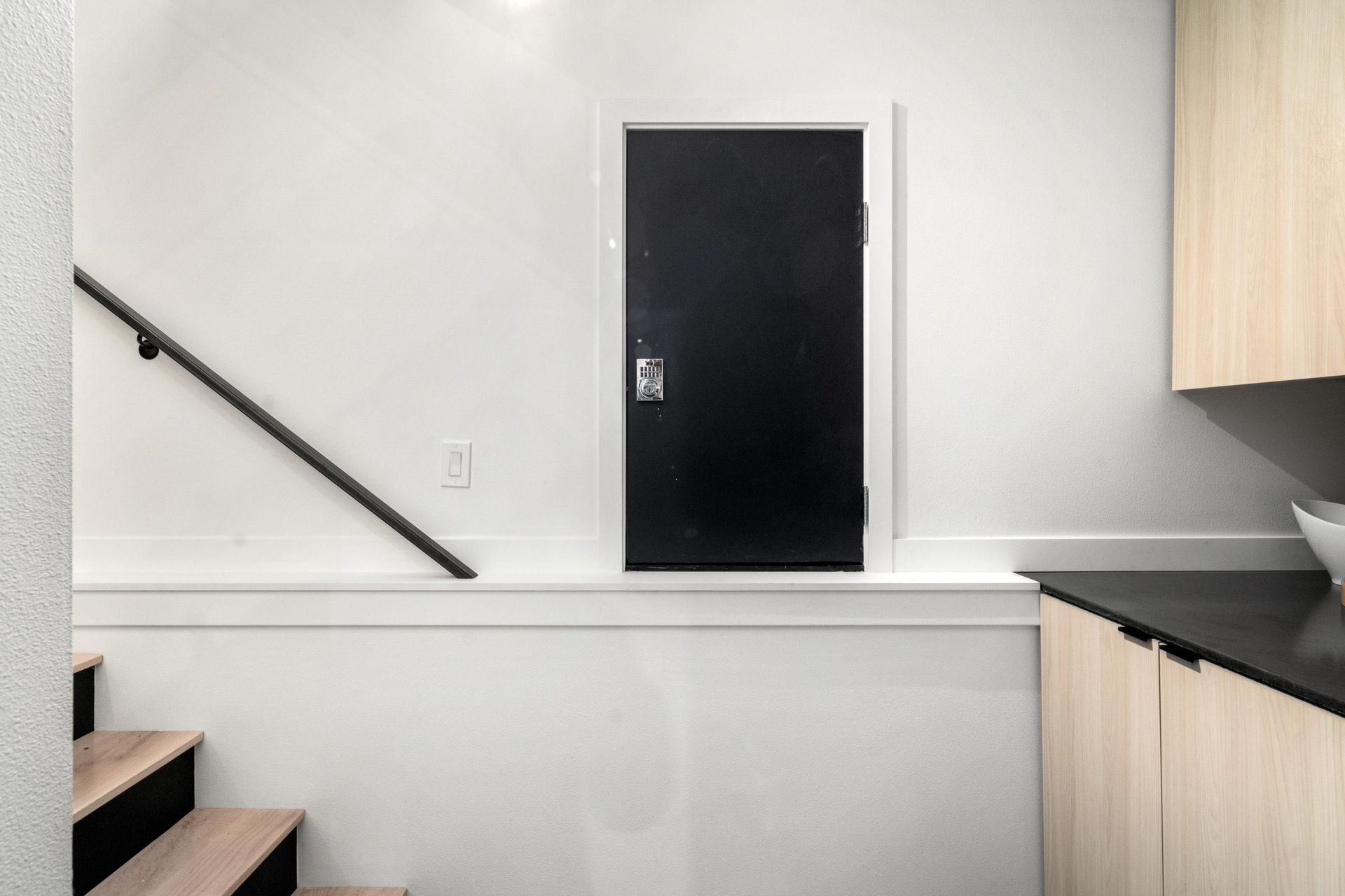 Small kitchen area with a black door centered on a white wall and a staircase railing on the left.