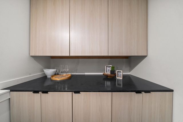 Modern kitchen countertop with black surface, light wood cabinets, and a bowl of fruit and small appliances.