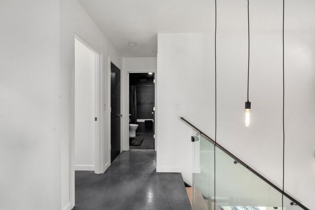 Modern white hallway with gray floor, glass staircase railing, and hanging light bulbs