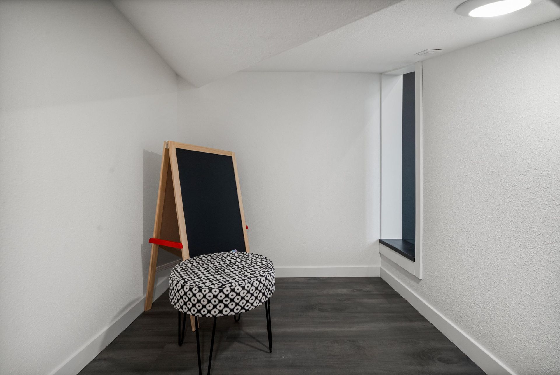 Small white room with a black patterned chair and a leaning framed blackboard.
