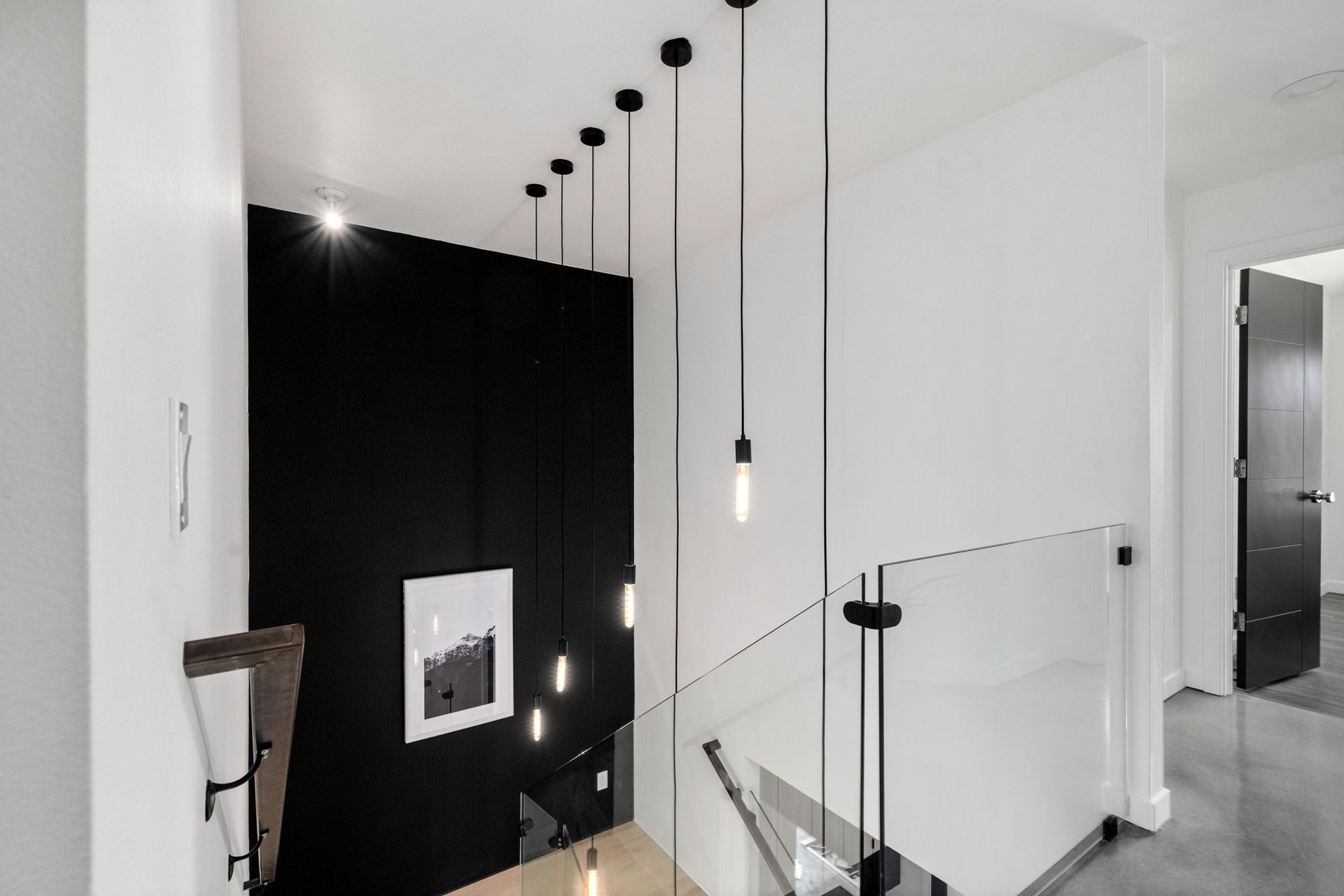 Modern staircase with black wall, hanging pendant lights, and glass railing in a minimalist interior