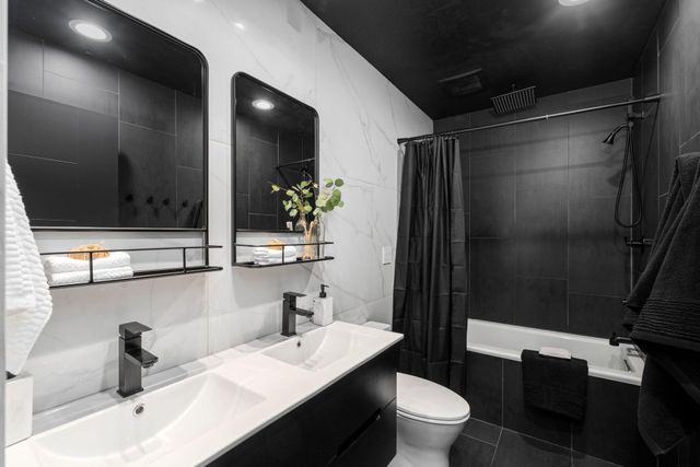 Modern black-and-white bathroom with double vanity, mirrors, toilet, and shower curtain