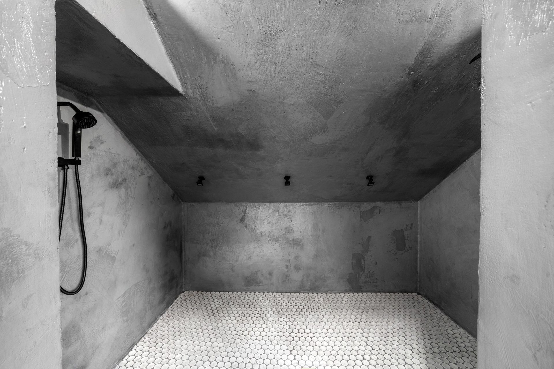 Empty gray shower stall with tiled floor and wall-mounted showerhead on the left