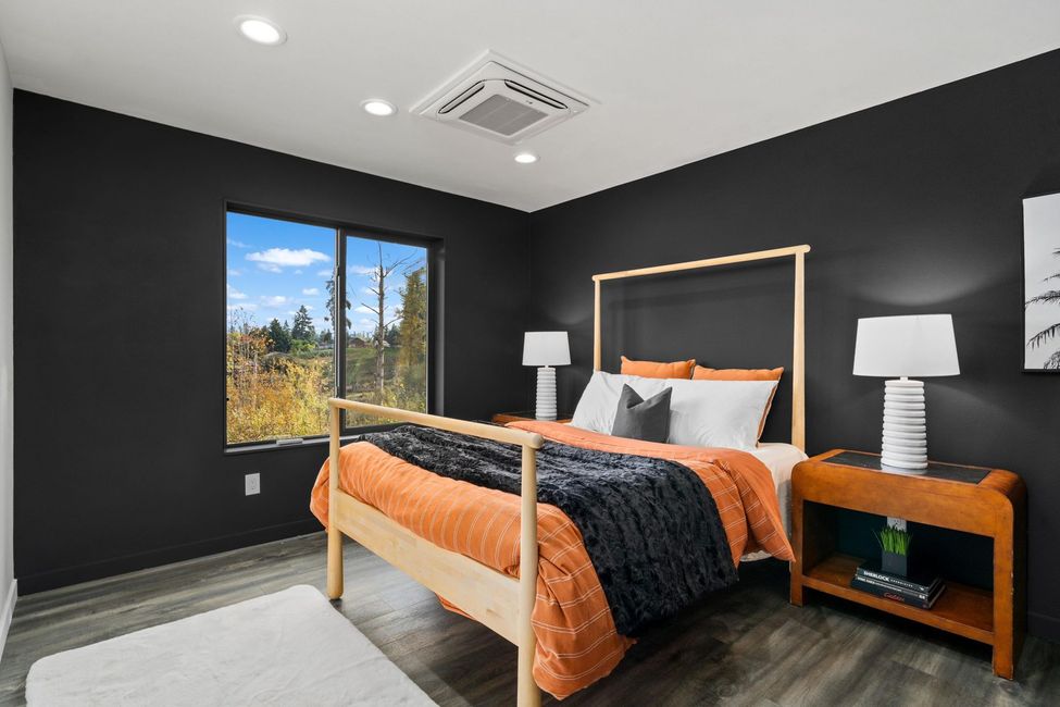 Modern bedroom with black walls, wood bed frame, orange bedding, and a large window with mountain view