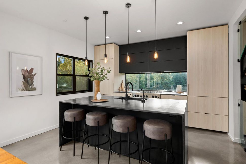 Modern kitchen with black island, pendant lights, bar stools, wood cabinets, and large windows