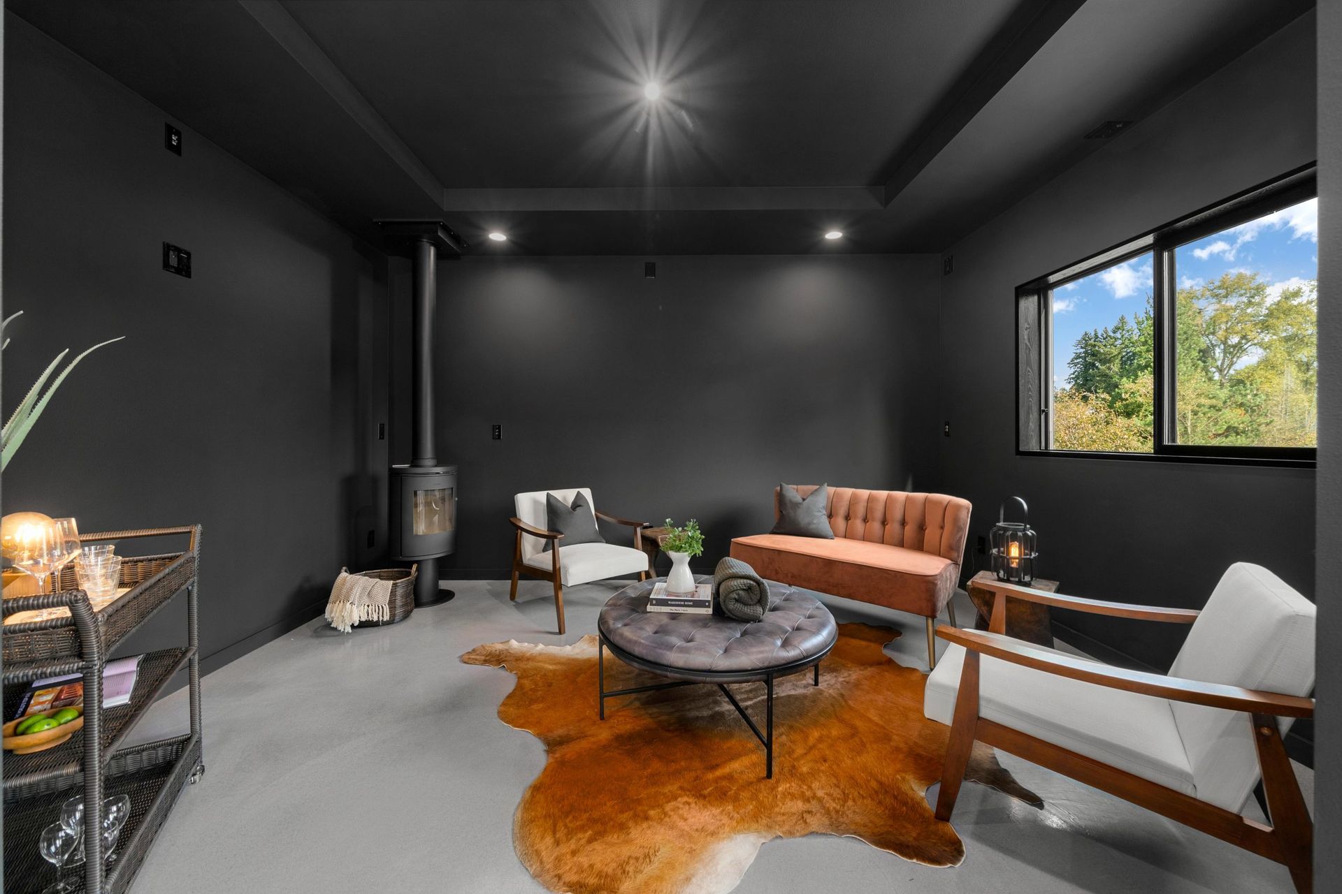 Modern living room with black walls, gray floor, orange sofa, white chair, and window view