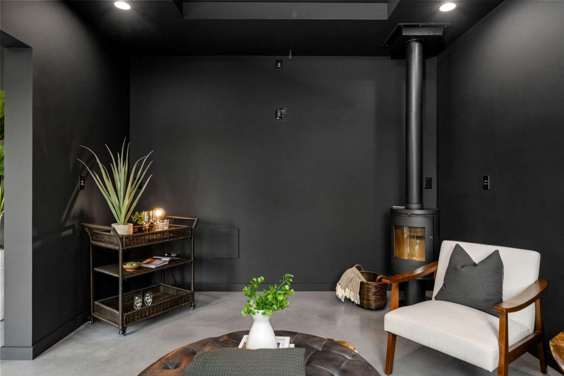 Cozy dark modern living room with wood stove, armchair, side table, and potted plant