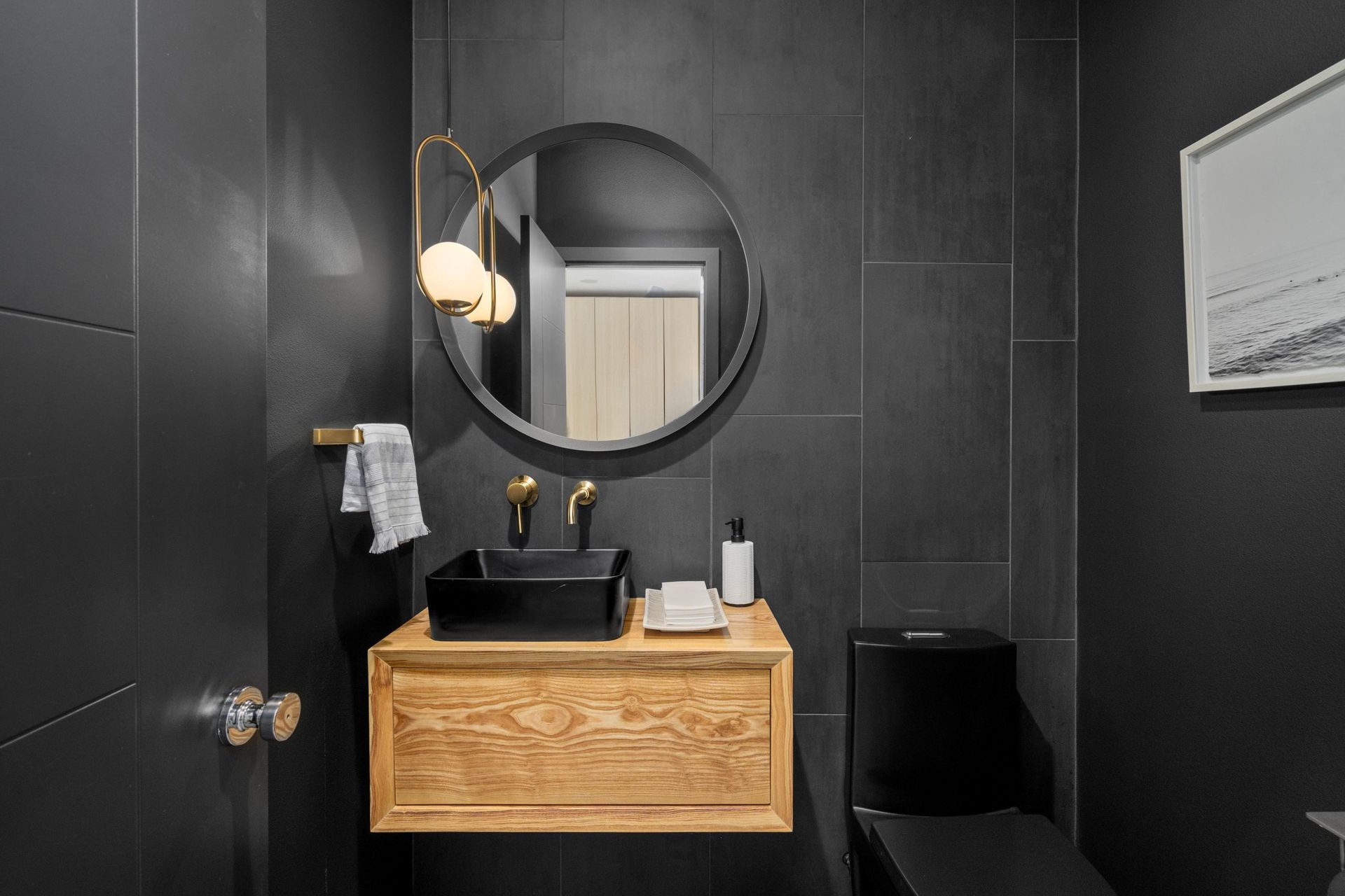 Modern black bathroom with round mirror, wooden vanity, and wall-mounted light fixture