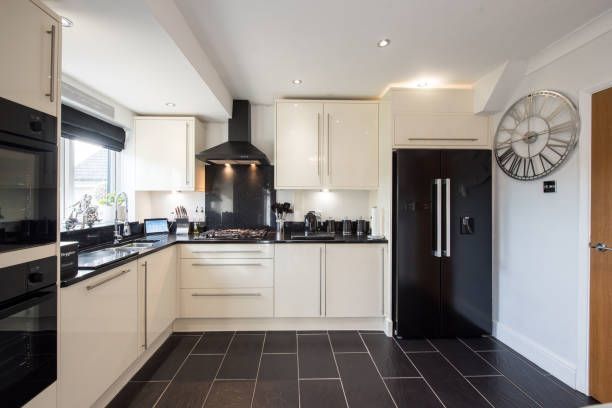 Cream-colored kitchen with black appliances, counters, and flooring. A large clock hangs on the wall.
