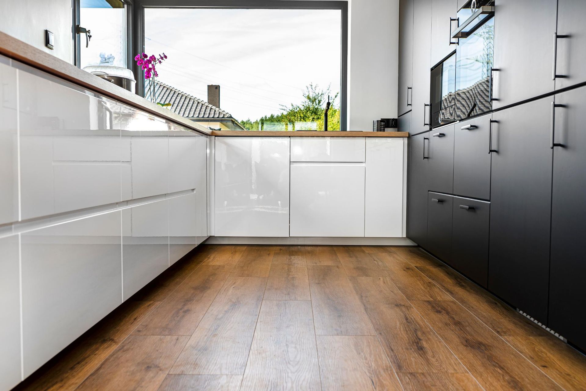 Modern kitchen with white and black cabinets, a large window, and wooden floors.
