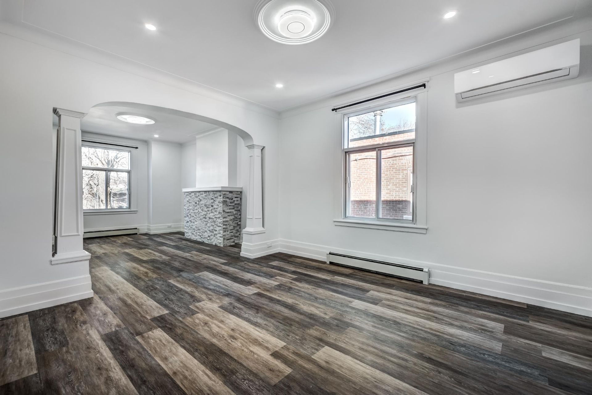 Empty renovated room with wood-look flooring, white walls, arched doorway, and a window.