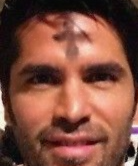 Man with ash cross on forehead; close-up. Smiling, brown eyes, dark hair, neutral background.