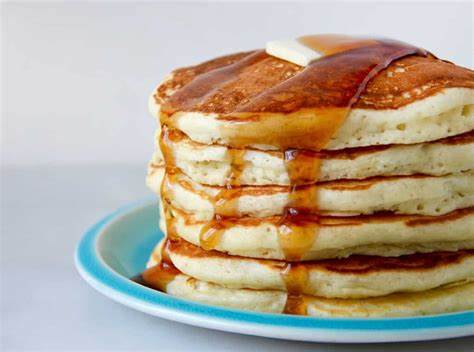 Stack of fluffy pancakes with syrup and butter on a blue plate.