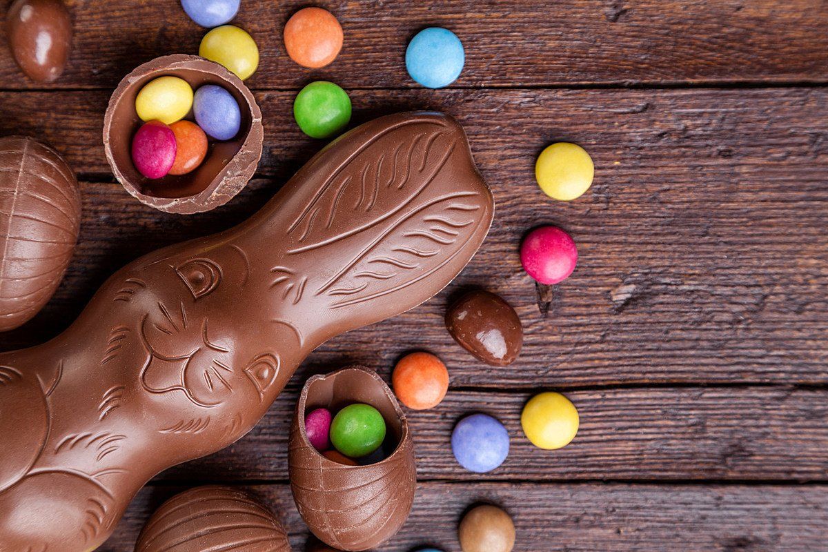 Chocolate Easter bunny with eggs and colorful candies on a wooden surface.