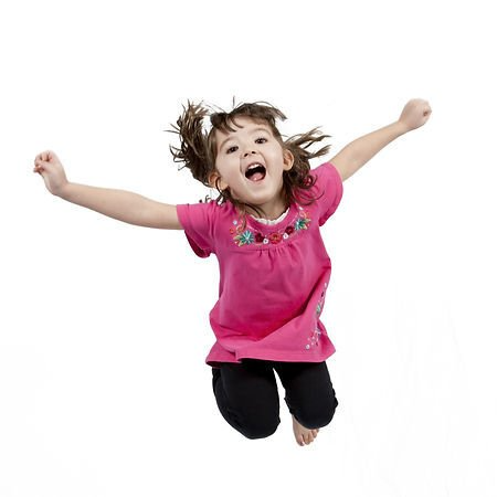 A child in a pink shirt and black pants jumps with arms raised and mouth open.