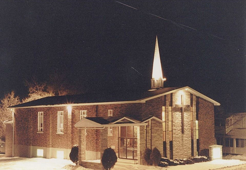 Church building at night, lit steeple, brick facade, windows, dark sky.