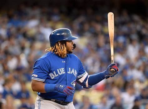 Baseball player in a blue uniform holding a bat, looking toward the field.