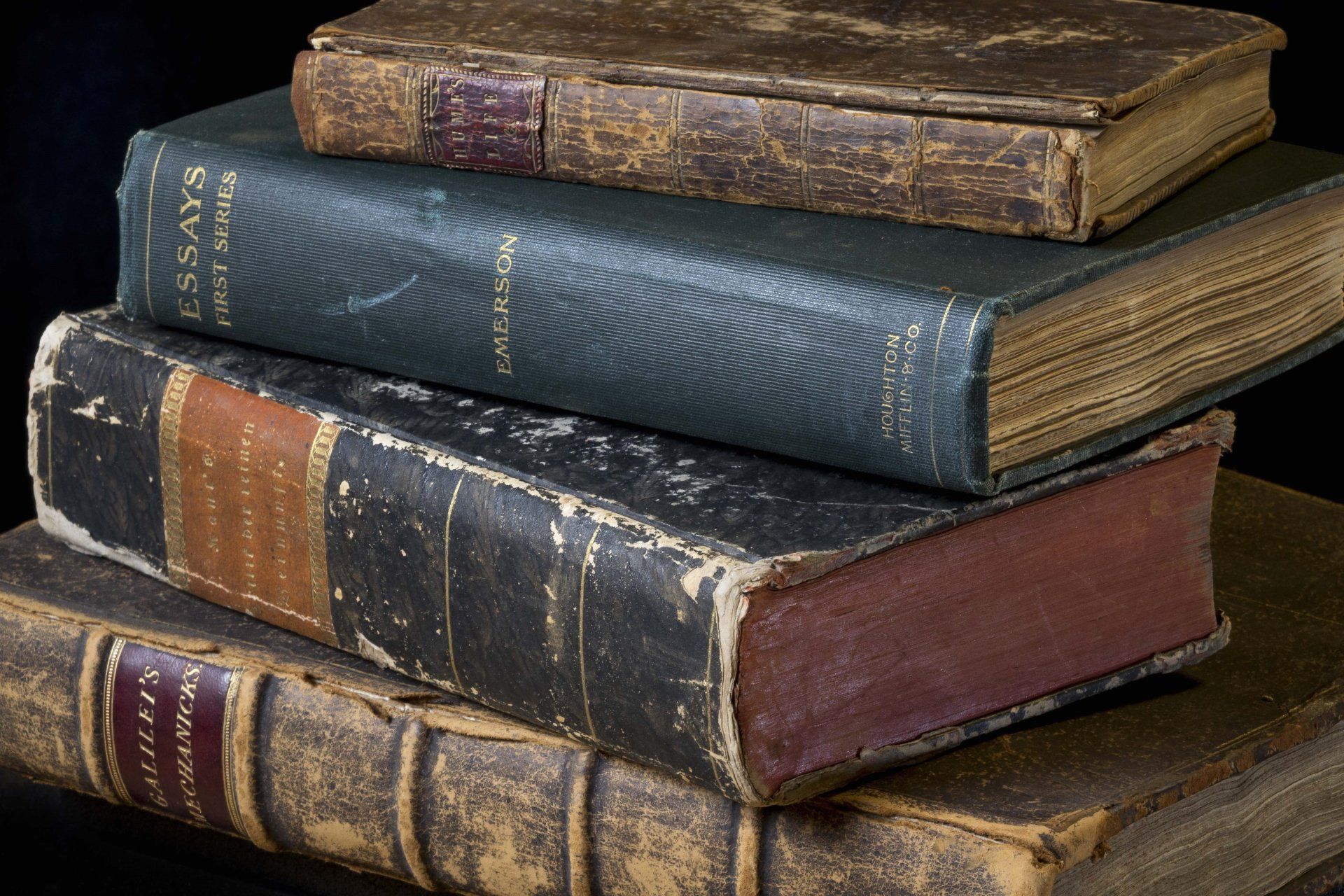 Pile of four old, leather-bound books; tan, brown, and dark green spines.