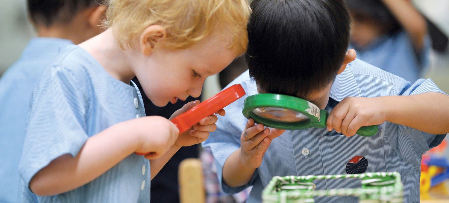 Two young children looking closely at an object with magnifying glasses.