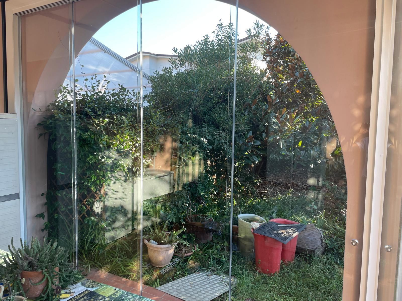 Spazio esterno ad arco con pannelli trasparenti, vista sul giardino.