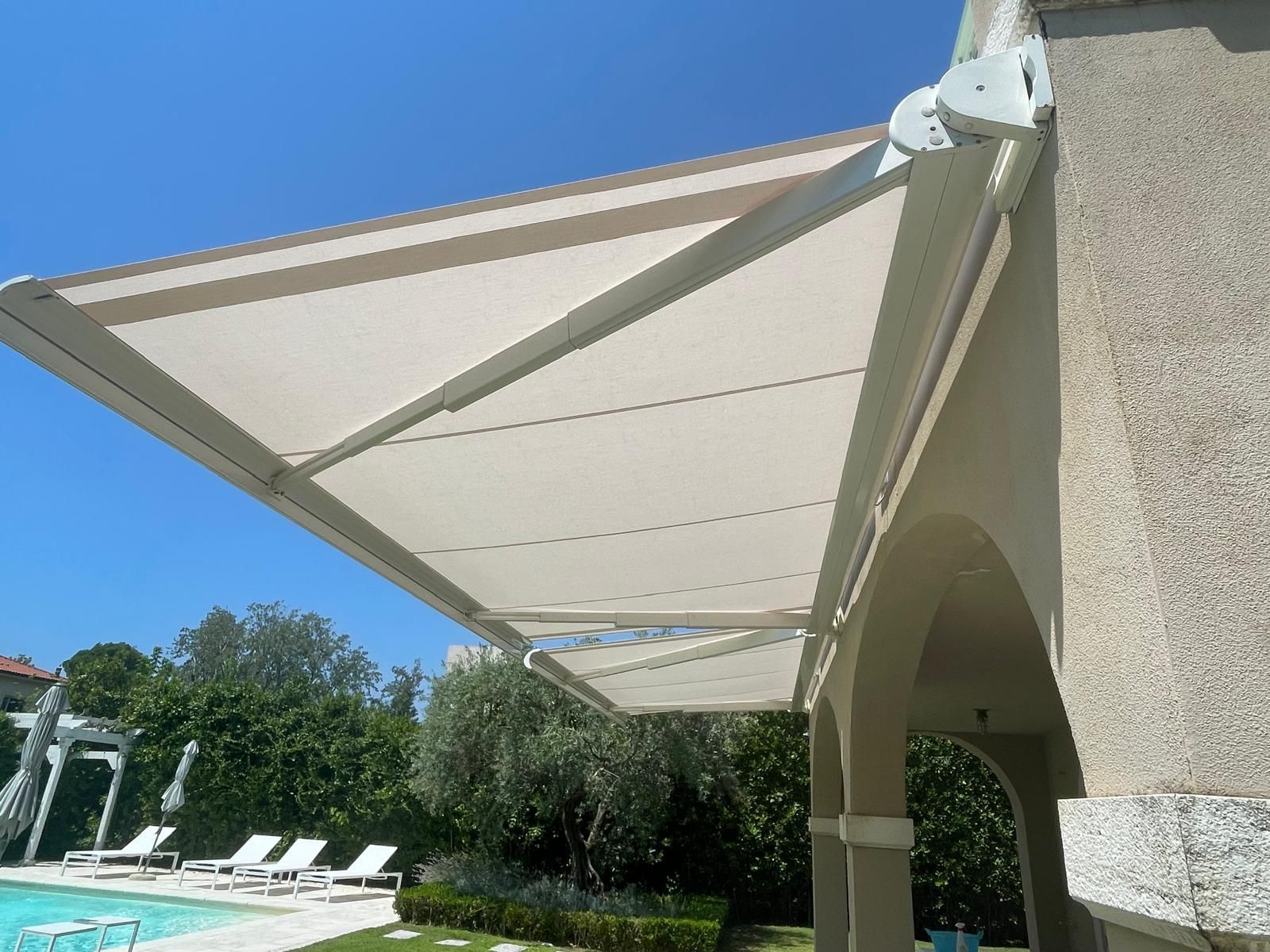 Una tenda da sole retrattile beige ripara il patio vicino alla piscina in una giornata di sole.