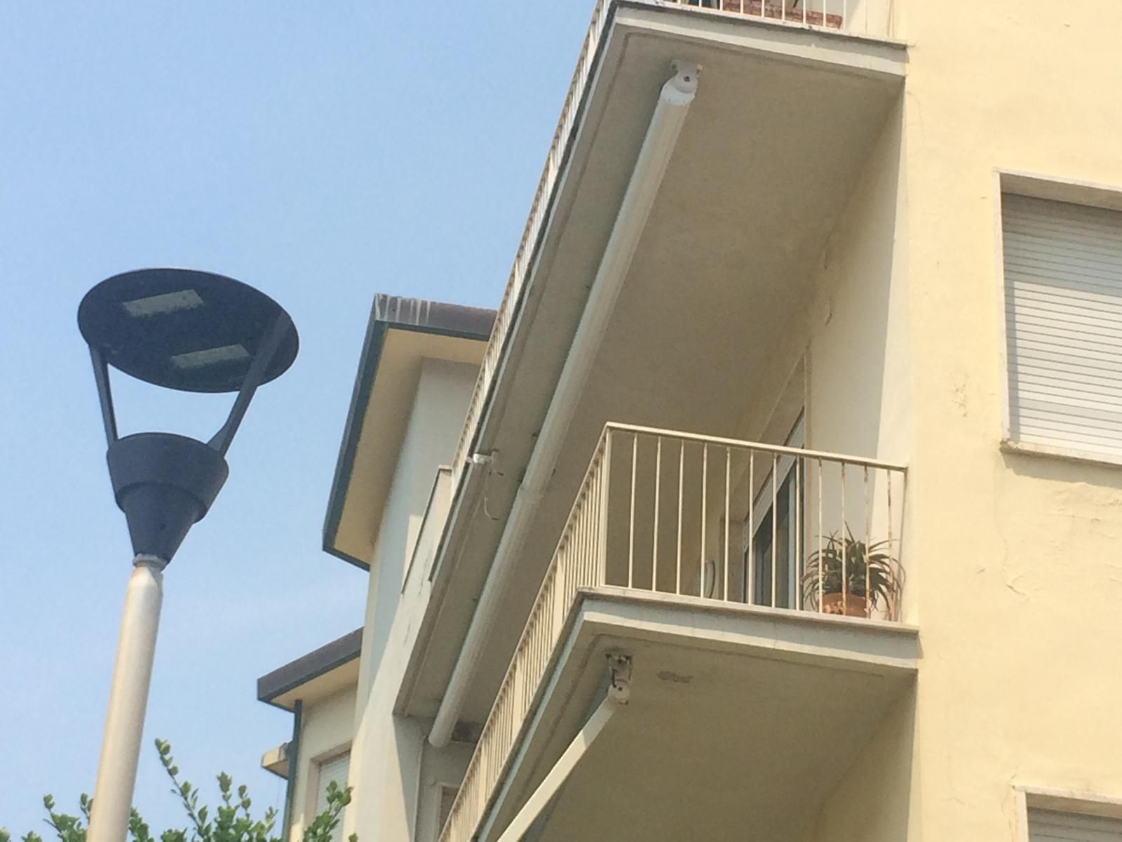 Lampione accanto a un edificio con balcone, sotto un cielo azzurro.