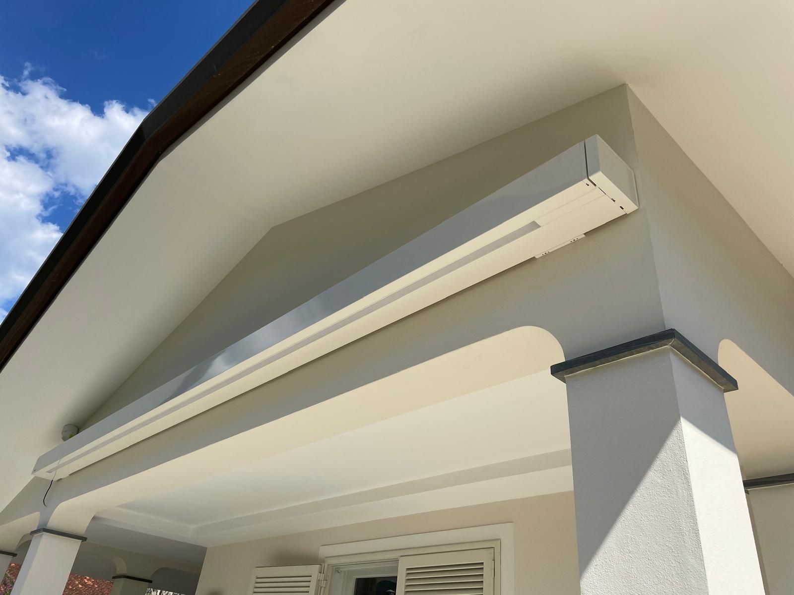 Esterno di un edificio con facciata e tetto bianchi. Una tenda da sole bianca è montata sopra la finestra.