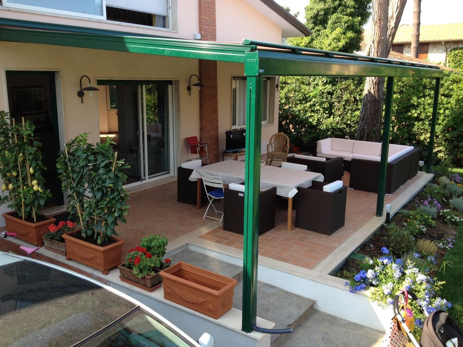 Pergola verde sopra un patio con tavolo da pranzo e posti a sedere; piante in vaso.