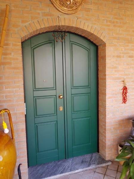 Doppie porte verdi inserite in un arco in mattoni. Un piccolo gradino ed elementi decorativi sopra le porte.