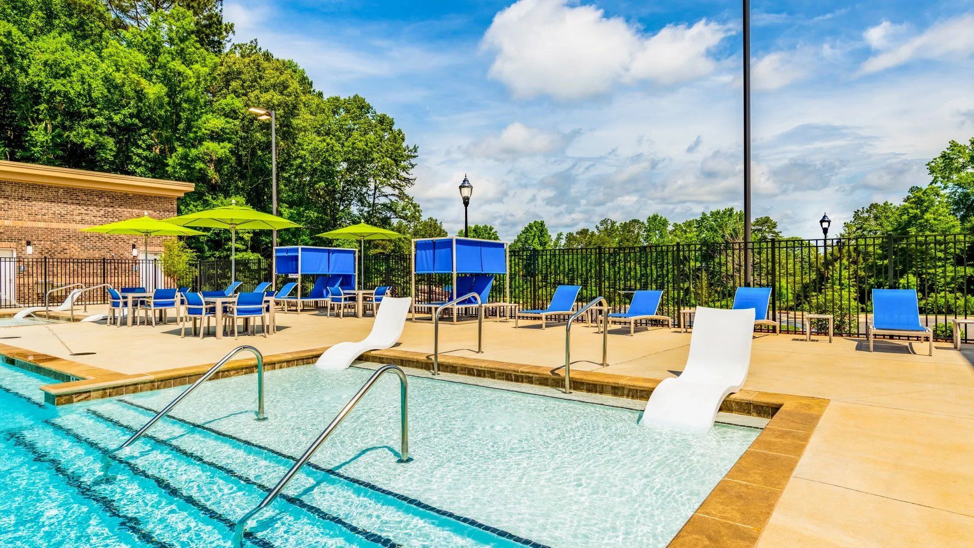 Swimming pool area with lounge chairs and umbrellas, surrounded by greenery. Our Wexhaw, NC apartments provide the best in luxury living in downtown Waxhaw. Ready to make our community your home? Contact Waxhaw Mills today to learn more and schedule your personalized tour! 
