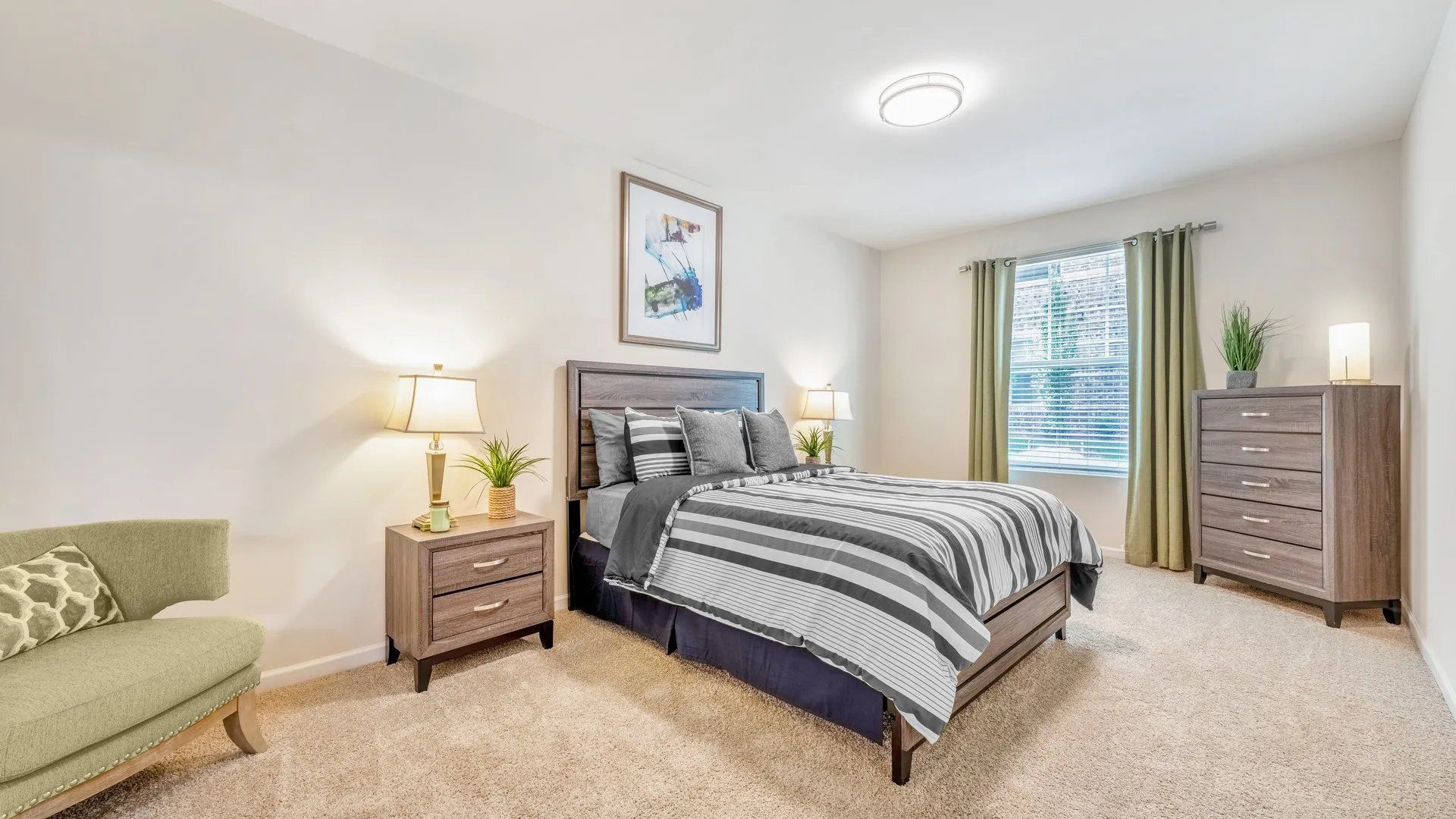 A well-decorated bedroom featuring a bed with striped bedding, a nightstand with a lamp, and a window with natural light. Interested in learning more about our 1, 2, and 3-bedroom apartments in Waxhaw, NC? Contact us today to schedule your tour!
