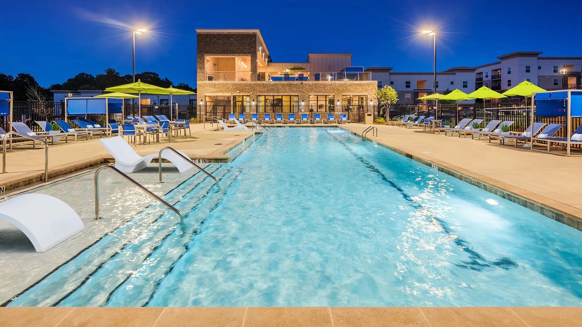 Community pool area with lounge chairs and vibrant umbrellas at night. Our Wexhaw, NC apartments provide the best in luxury living in downtown Waxhaw. Ready to make our community your home? Contact Waxhaw Mills today to learn more and schedule your personalized tour! 