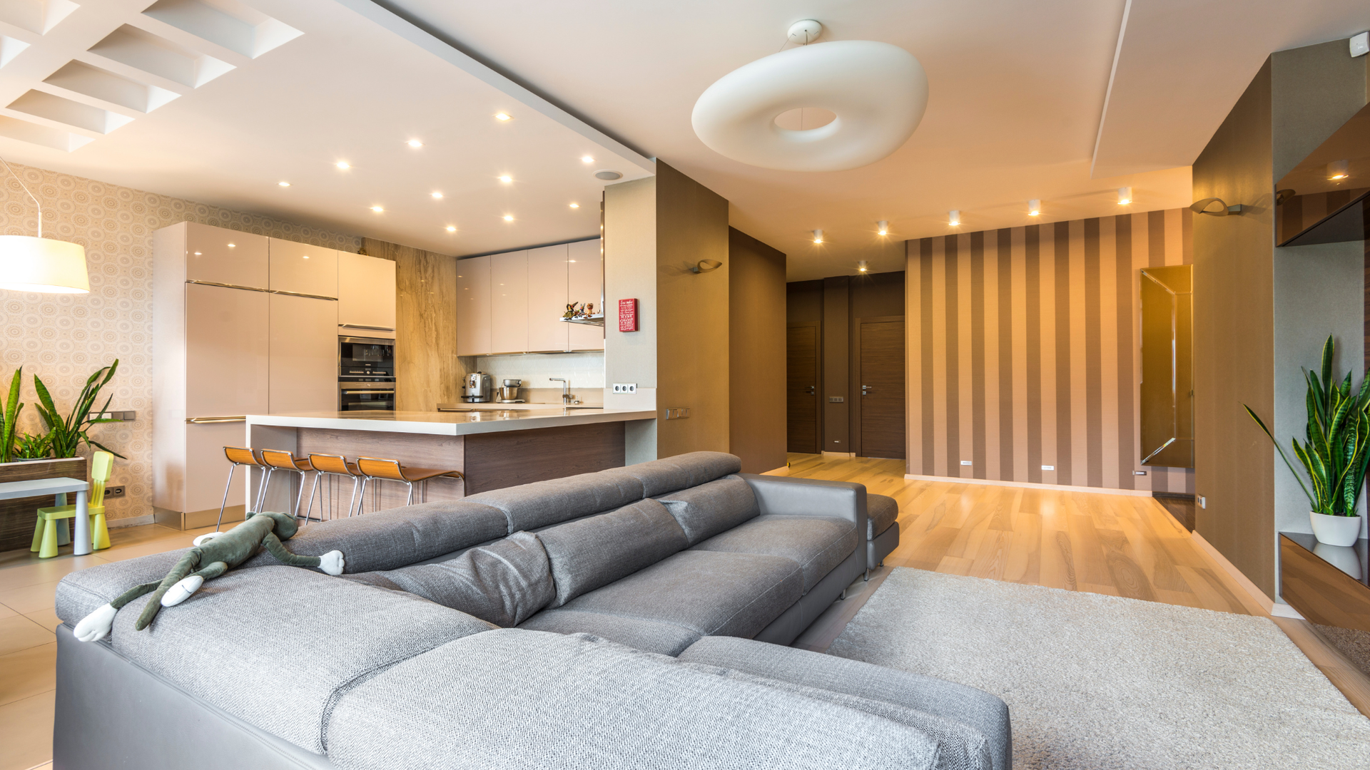 Modern open-plan living room with gray sectional sofa, kitchen island, and warm wood accents