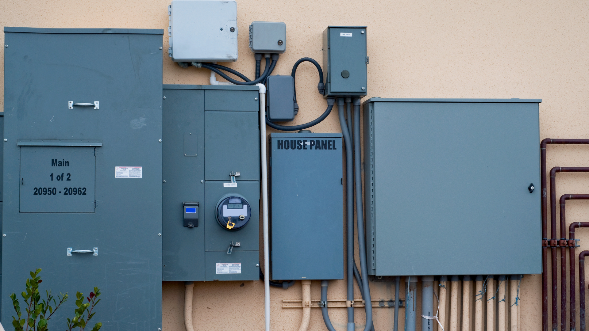 Blue utility meters and electrical boxes mounted on a building wall with visible conduit and cables