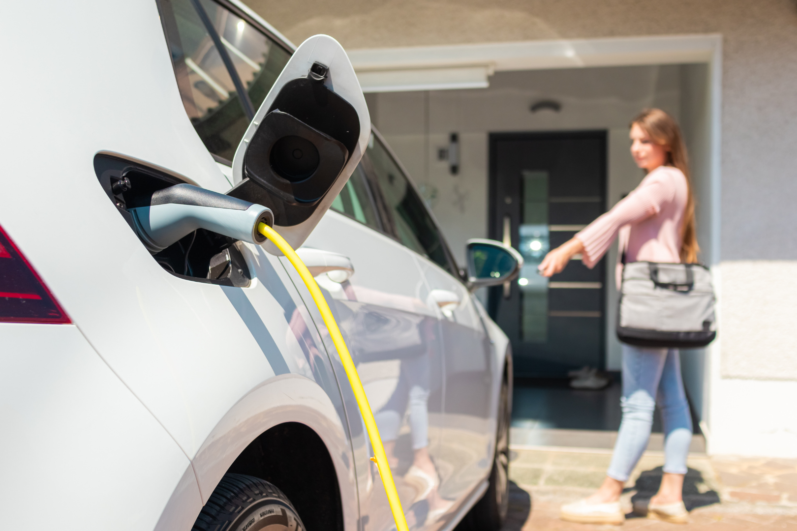 Electric car charging at a home driveway while a person opens the front door nearby.