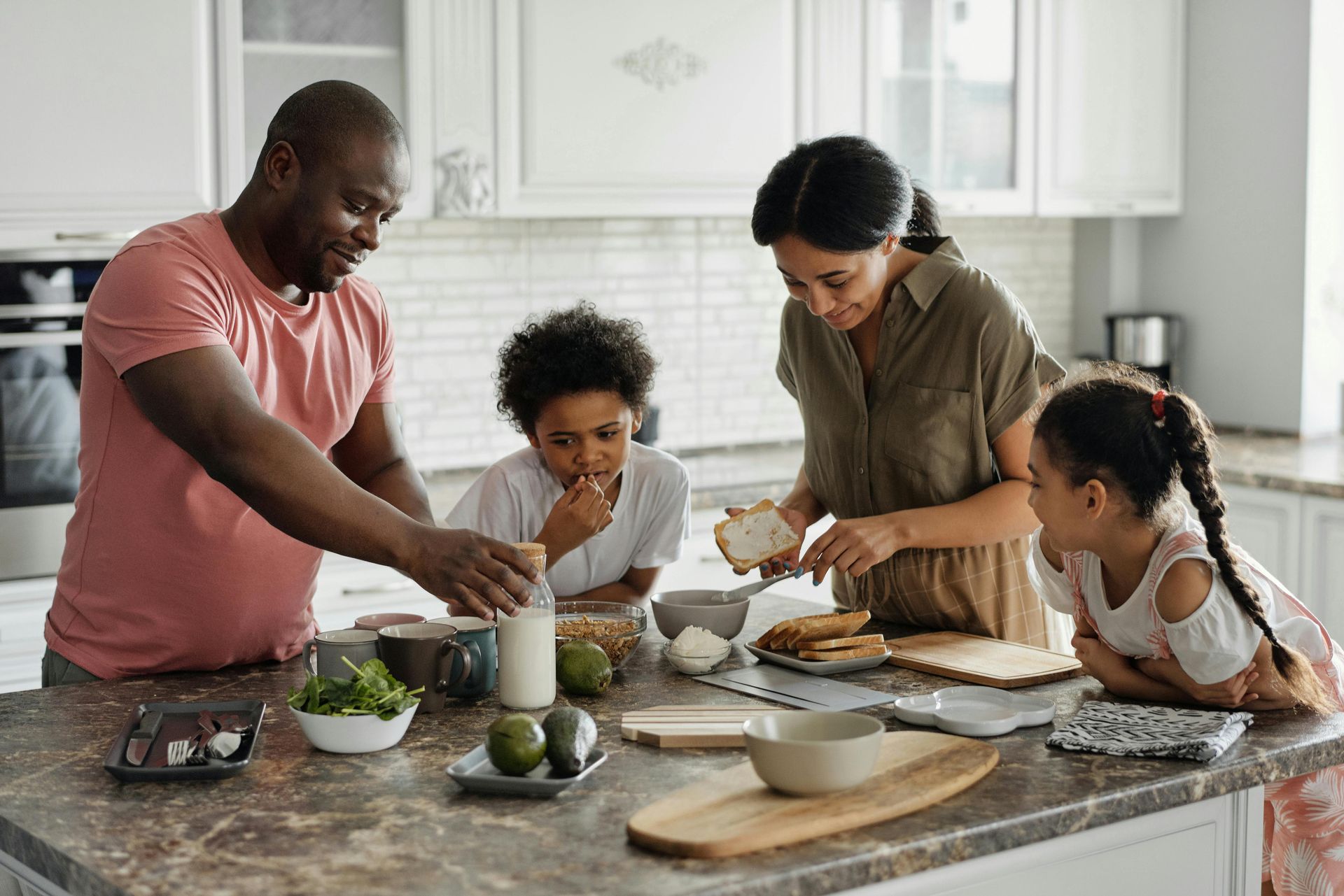 Family preparing food in a kitchen. Adults and children are interacting near a countertop with ingredients.