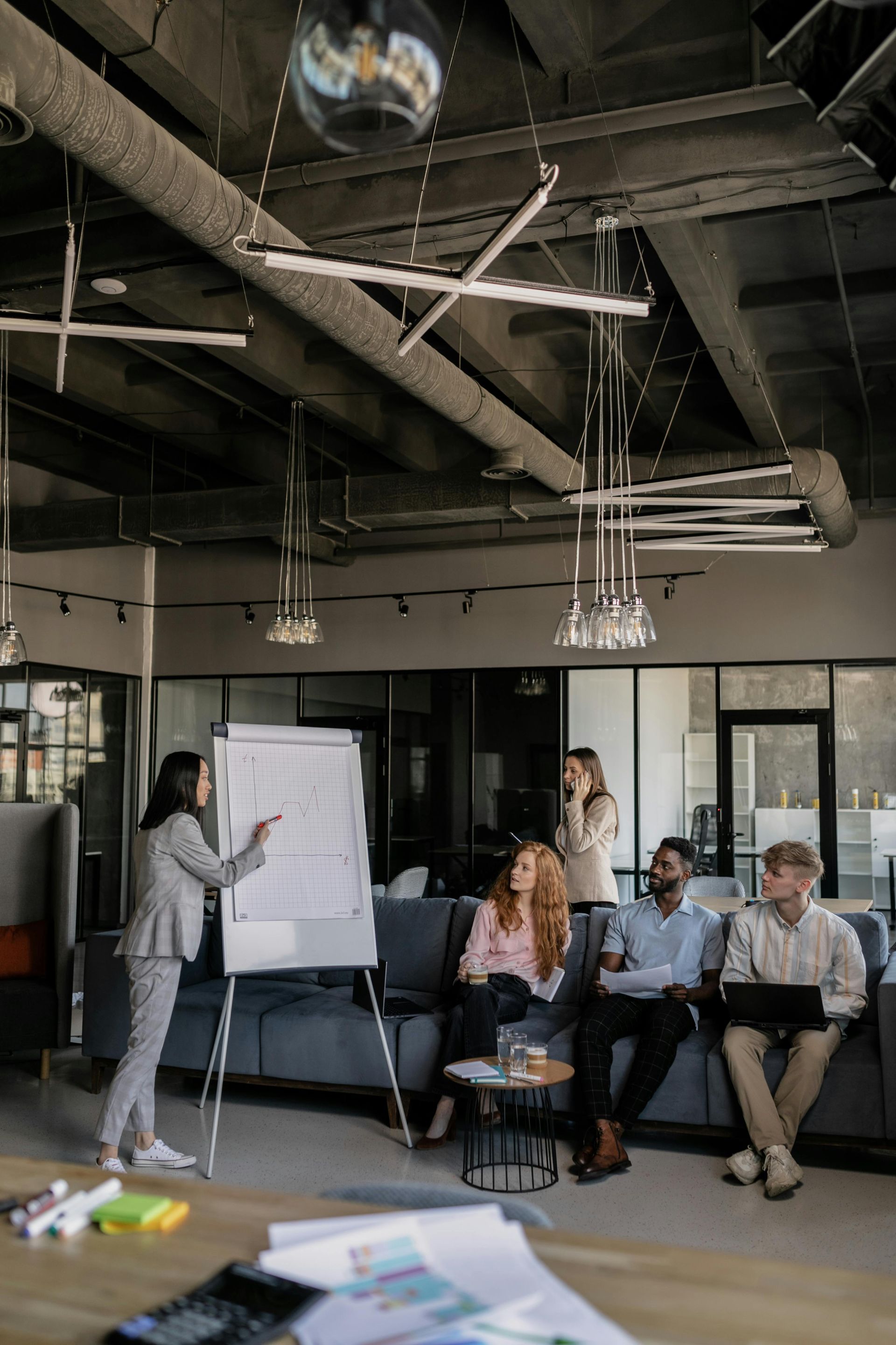 Woman presents at a whiteboard in an office setting, with a seated audience observing.