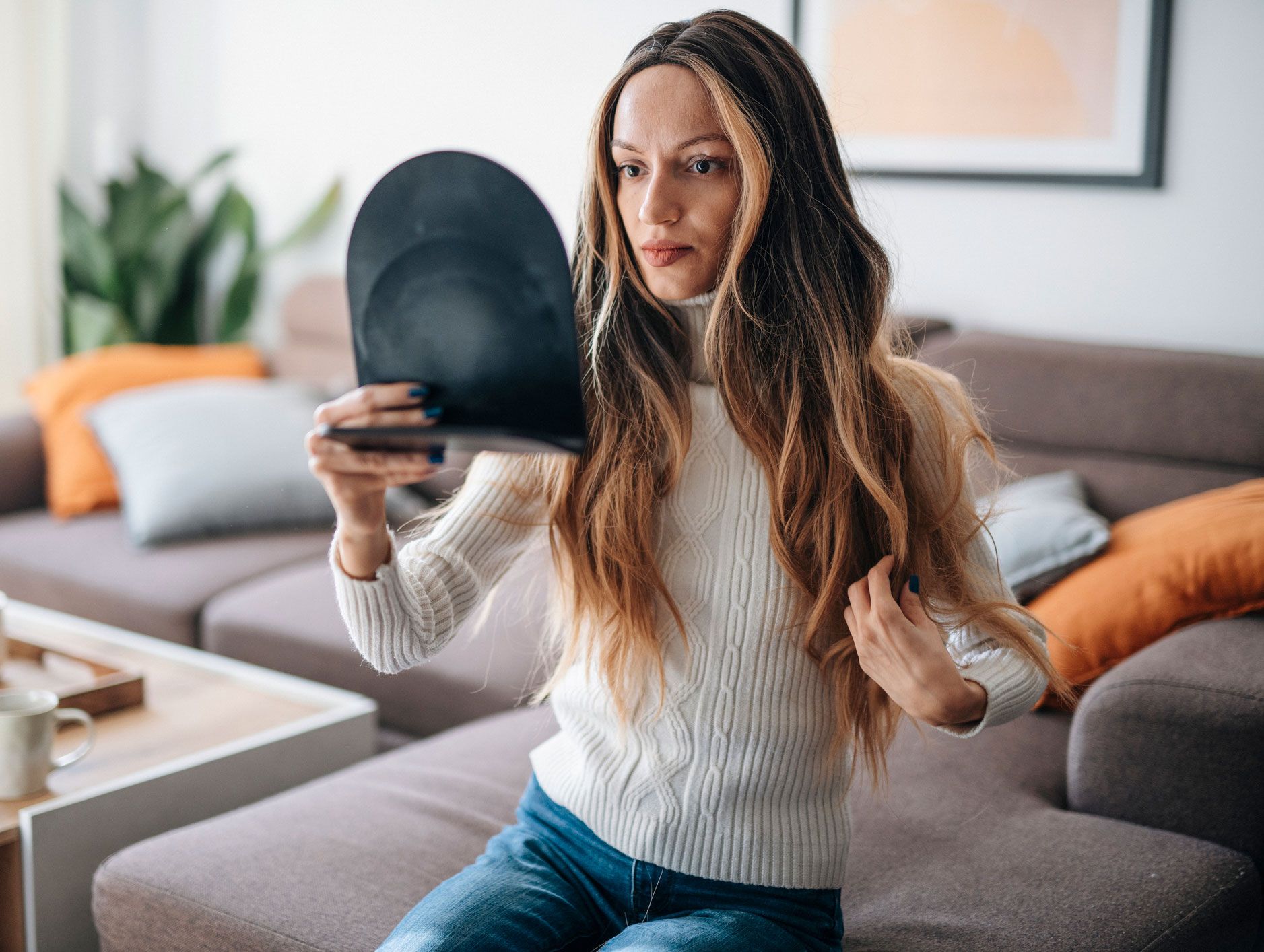 A woman is sitting on a couch looking at her hair in a mirror. A woman is sitting on a couch looking at her hair in a mirror.