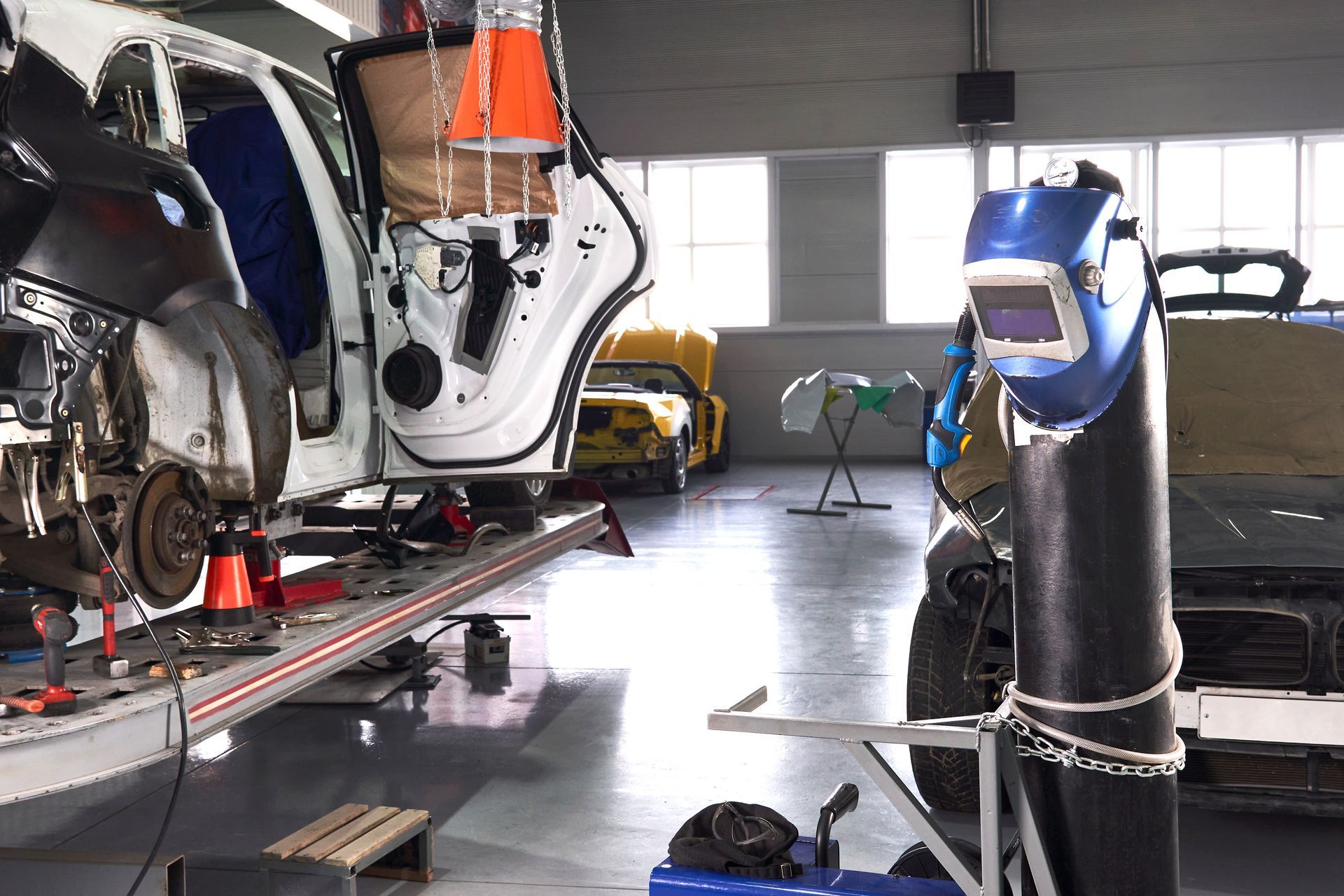 A car is being repaired in a garage with a welding helmet.