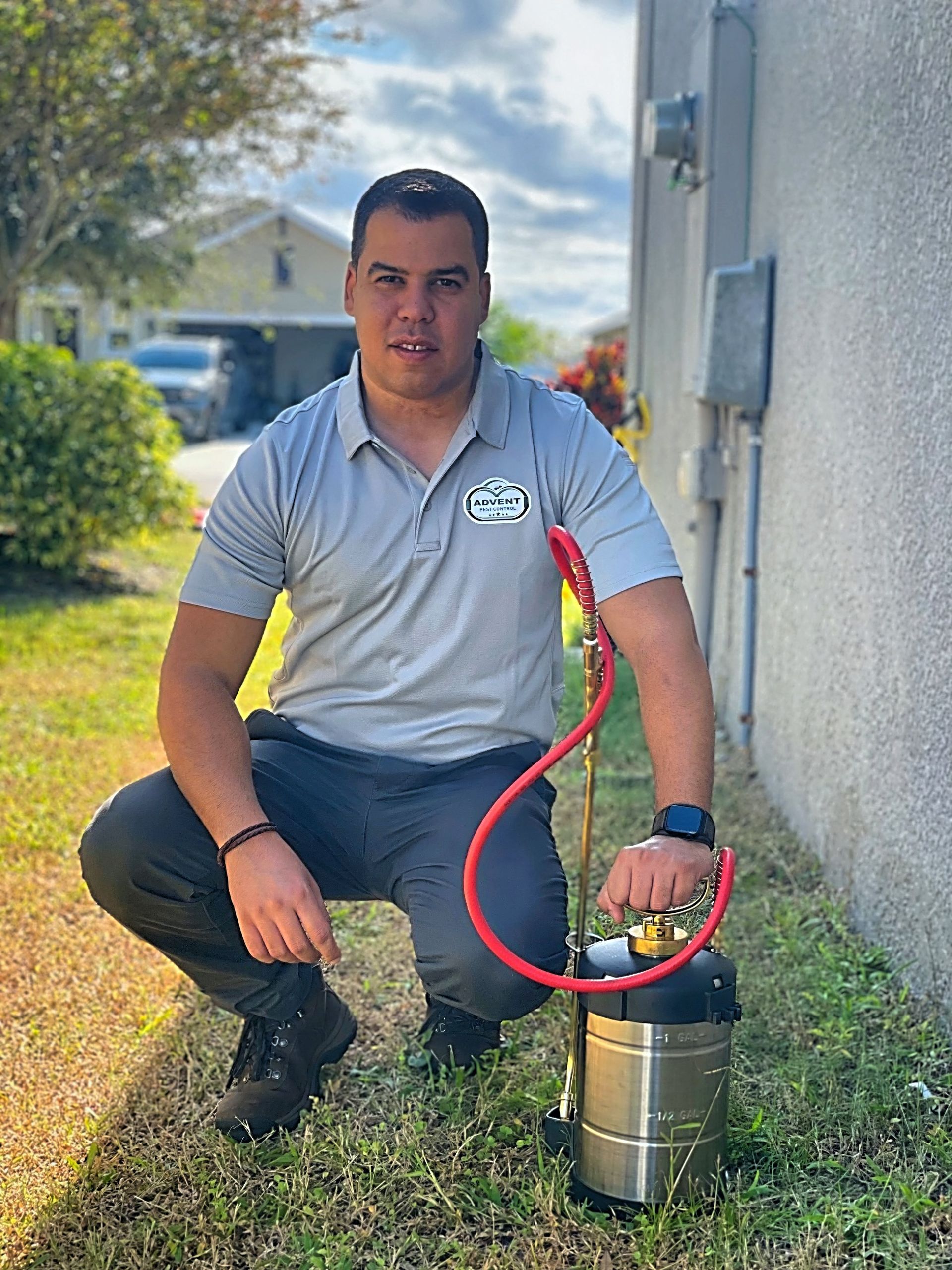 A man is kneeling down in the grass holding a sprayer.