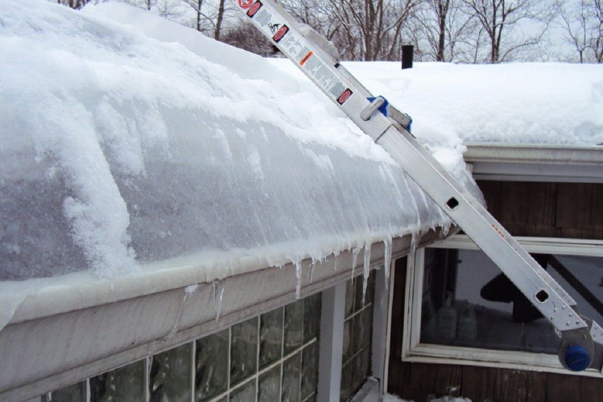 Ladder leaning against a roof with heavy snow and icicles hanging from the eaves.