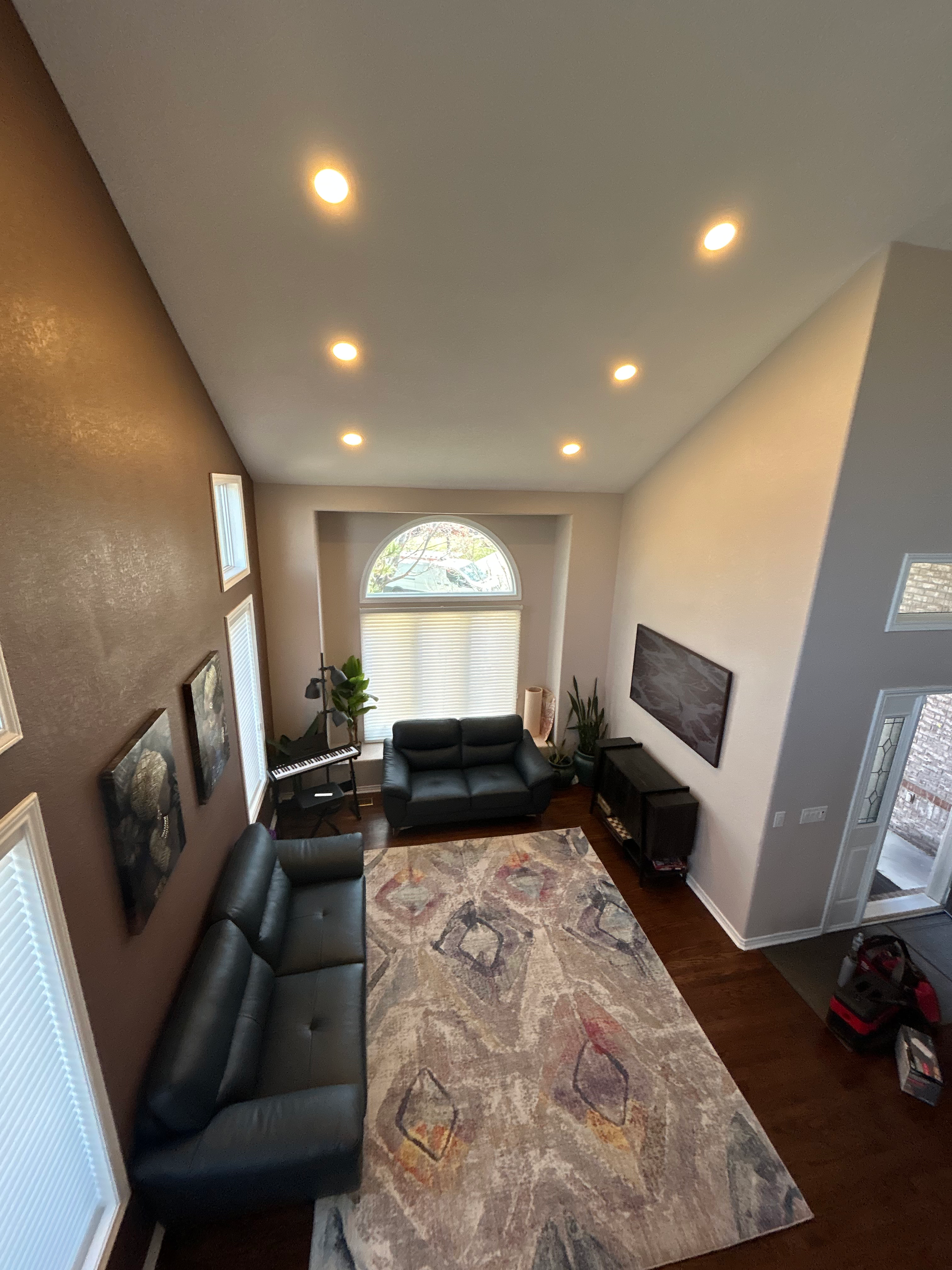 High-angle view of a living room with a gray, patterned rug, black couches, and recessed lighting.