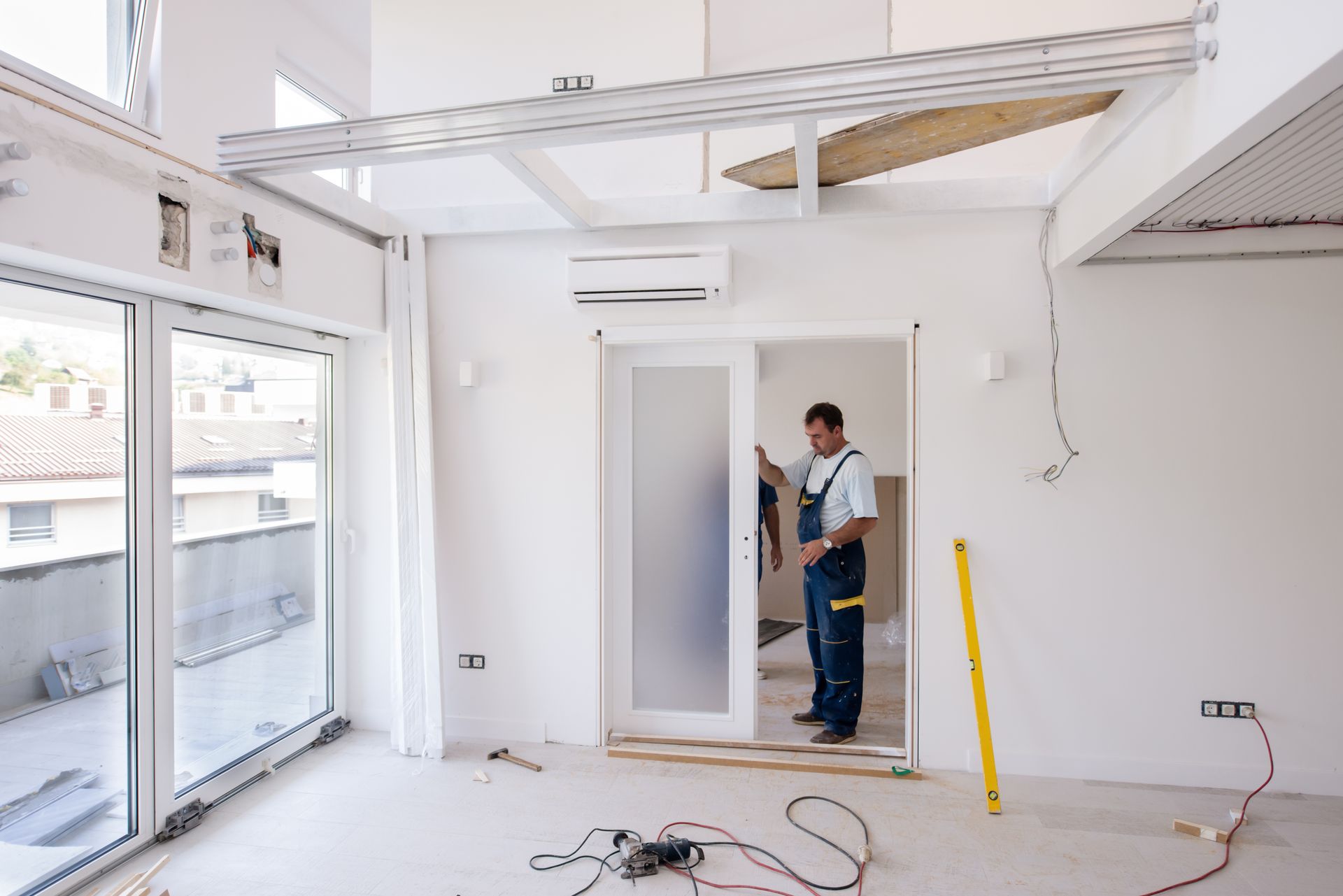 A worker installing a frosted glass sliding door in a bright, white interior during renovations. A worker installing a frosted glass sliding door in a bright, white interior during renovations.